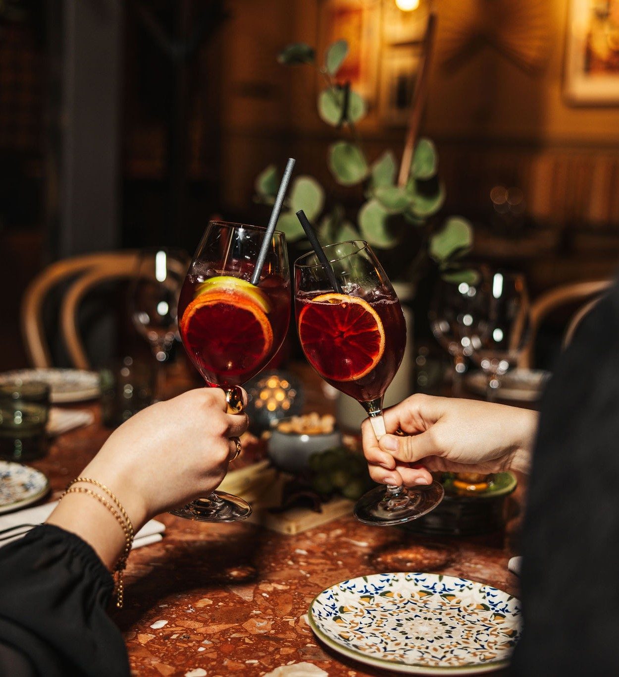 Två gäster skålar med sangriaglas garnerade med blodapelsin